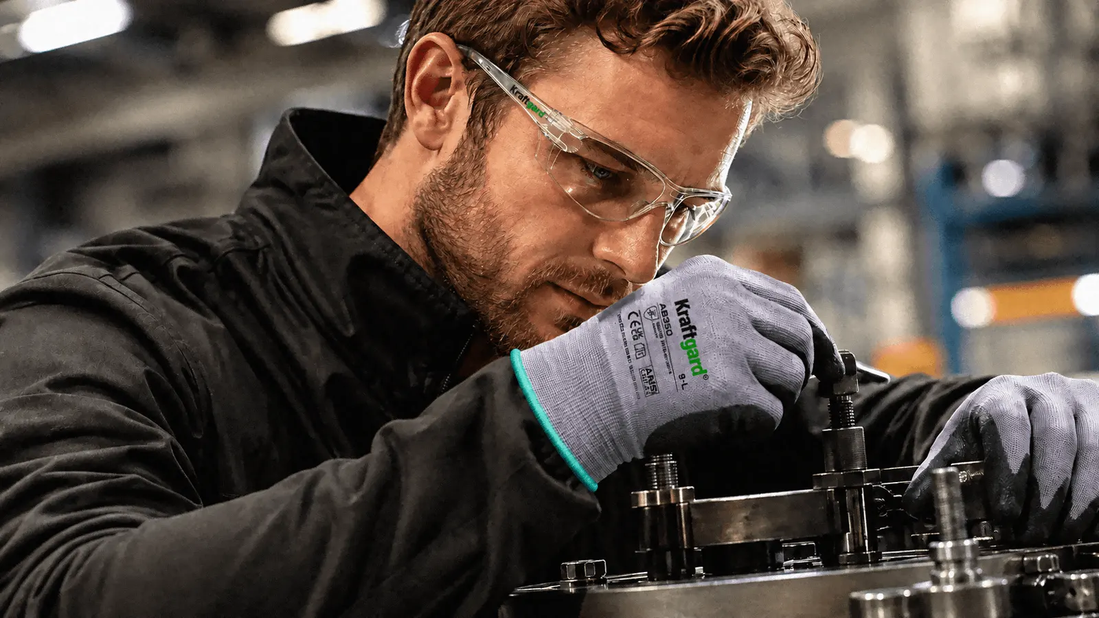 Industriarbetare med Kraftgard skyddsglasögon och handskar monterar en maskindel.